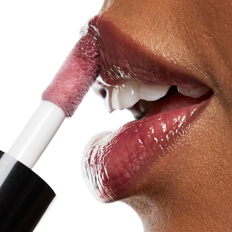 Thick doe foot applicator of Mary Kay Tinted Lip Oil in Berry being applied to lips on deep skin-toned woman with a white background&nbsp;