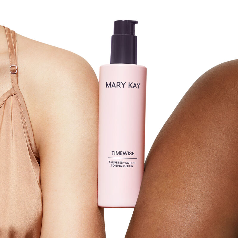 Bottle of TimeWise Targeted-Action Toning Lotion being held between medium skinned and deep skinned shoulders against light pink background