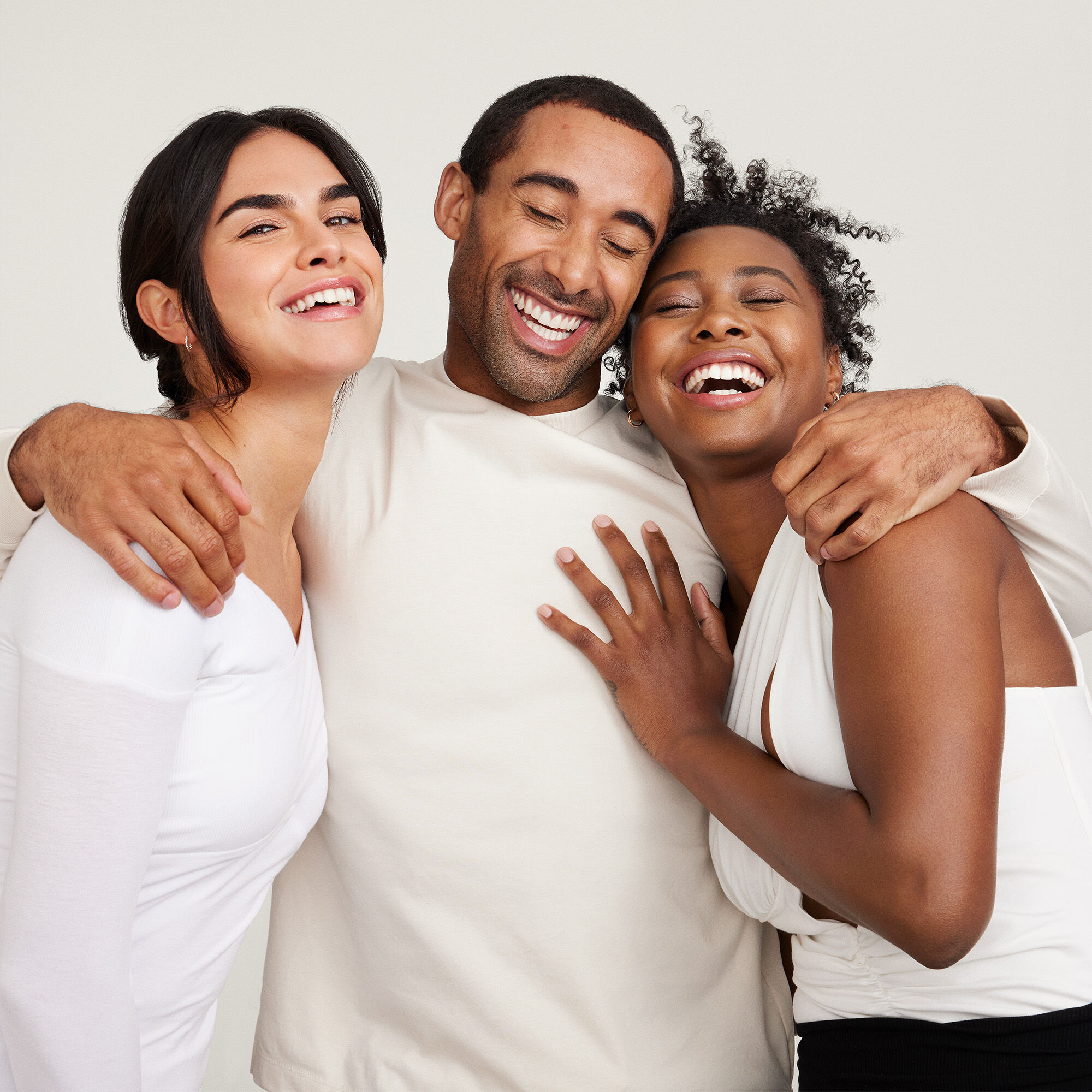 Tres personas abrazadas sobre un fondo neutro.
