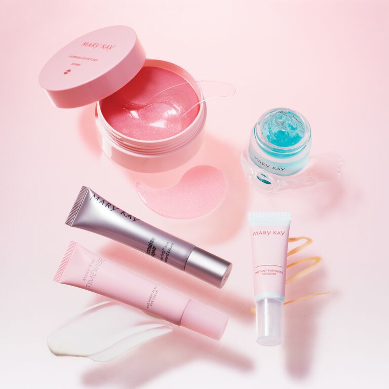 Mary Kay skincare products including eye patches, gel mask, and tubes arranged on a pink surface