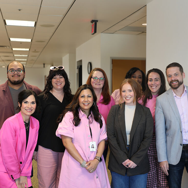 Group of employees standing together in office hallway wearing pink and business attire