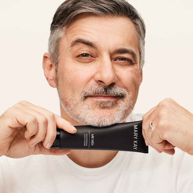 Hombre sonriendo y sosteniendo un tubo de Crema de Afeitar Hidratante MKMen&reg; junto a la barbilla